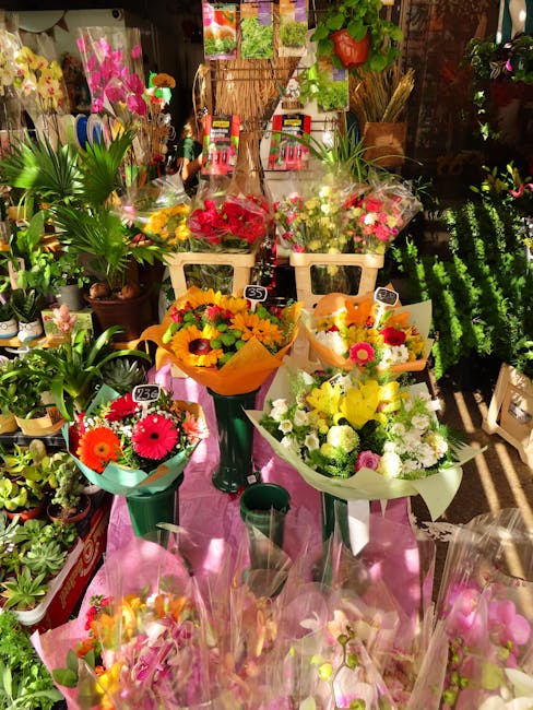 A display of freshly arranged floral bouquets at a flower shop, featuring vibrant blooms including pink, yellow, orange, and white flowers, wrapped in colorful paper and set on a pink cloth-covered ta