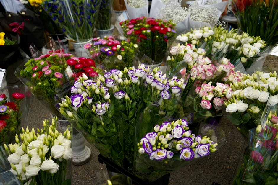 A vibrant display of fresh flower bouquets arranged on a countertop, featuring various blooms including purple and white lisianthus, pink and white roses, and small pink chrysanthemums. The flowers ar